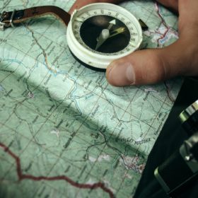 traveler exploring map with compass in sunny forest in the mountains